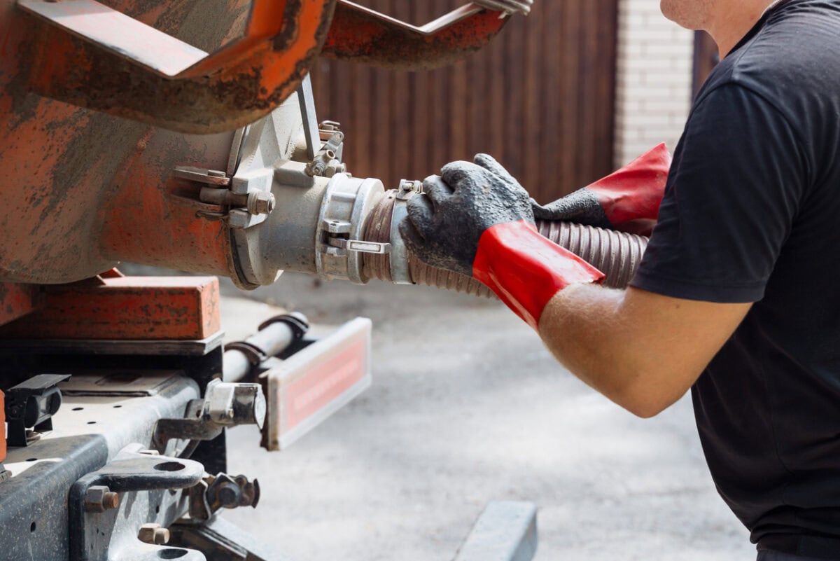 technician performing a septic pump out by connecting a vacuum hose to a septic service truck